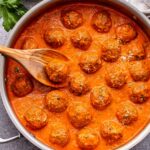 Turkey Meatballs in Roasted Red Pepper Sauce in a metal skillet with a wooden spoon in it.