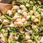 Asparagus goat cheese pasta in a white bowl with a wooden spoon.