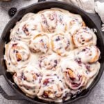 12 Blackberry Vanilla Sweet Rolls in a cast iron skillet topped with cream cheese frosting.