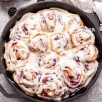 12 Blackberry Vanilla Sweet Rolls in a cast iron skillet topped with cream cheese frosting.