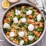 metal skillet with spicy sausage and broccoli pasta in it. Pasta topped with dollops of ricotta cheese. A small bowl of ricotta behind the skillet and half of a lemon.