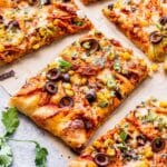 Chicken enchilada pizza cut into slices on top of parchment paper.