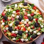 Berry Pesto Pasta Salad made with strawberries, blackberries, arugula and mozzarella balls in a white serving bowl. A small bowl of balsamic glaze behind the salad.