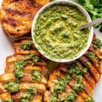 White plate with three chicken breasts on it and a bowl of chimichurri.