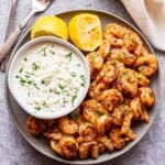 gray plate with grilled spicy shrimp and feta dip on it and two lemon halves.