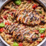 stainless steel pan filled with Tomato Basil Pasta with sliced Balsamic Grilled Chicken on top of it.