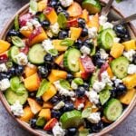 Blueberry Peach Feta Salad in a white serving bowl with two spoons and a bowl of the vinaigrette behind it.
