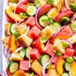 Watermelon Peach Panzanella Salad with cucumbers, red onion and basil on a white serving platter.
