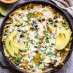 Green Chile Chicken Enchiladas in a cast iron skillet topped with avocado slices and melted cheese.