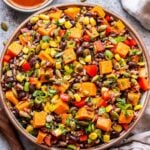 Southwest Sweet Potato, Black Bean, Wild Rice Salad in a white bowl with chili lime vinaigrette behind it.