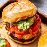 Chicken Fajita Burger topped with peppers, onions and guacamole with a bowl of guacamole behind the burger.