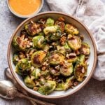 Miso roasted brussels sprouts in a white bowl with a bowl of dressing behind it.
