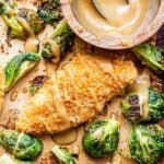 Parmesan chicken and brussels sprouts on a sheet pan with a bowl of honey mustard sauce. Sauce is drizzled over the chicken and brussels sprouts.