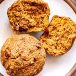 two pumpkin apple muffins on a white plate. One is broken in half