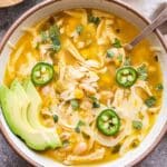 White Chicken Chili in a white bowl with a spoon and a small bowl of lime wedges behind it.