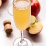 Apple Cider Mimosa with a champagne cork and apples behind it.