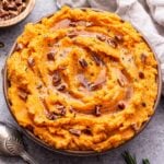 Brown Butter Mashed Sweet Potatoes in a serving bowl with a spoon next to them and a bowl of pecans behind it.