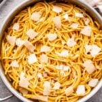 Pumpkin cacio e pepe in a skillet with a wedge of pecorino cheese at the bottom and a pepper grinder behind the skillet..