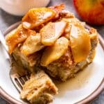 A piece of Apple Cinnamon French Toast Casserole on a white plate with a bite on a fork.