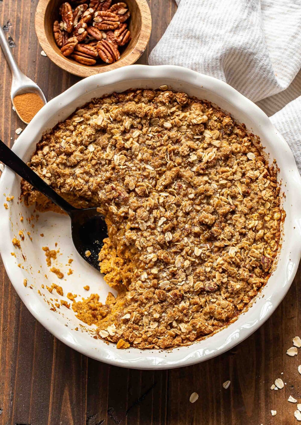 Pumpkin crisp in a white pie dish with a scoop cut out and black serving spoon in it's place.