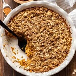 Pumpkin crisp in a white pie dish with a scoop cut out and black serving spoon in it's place.