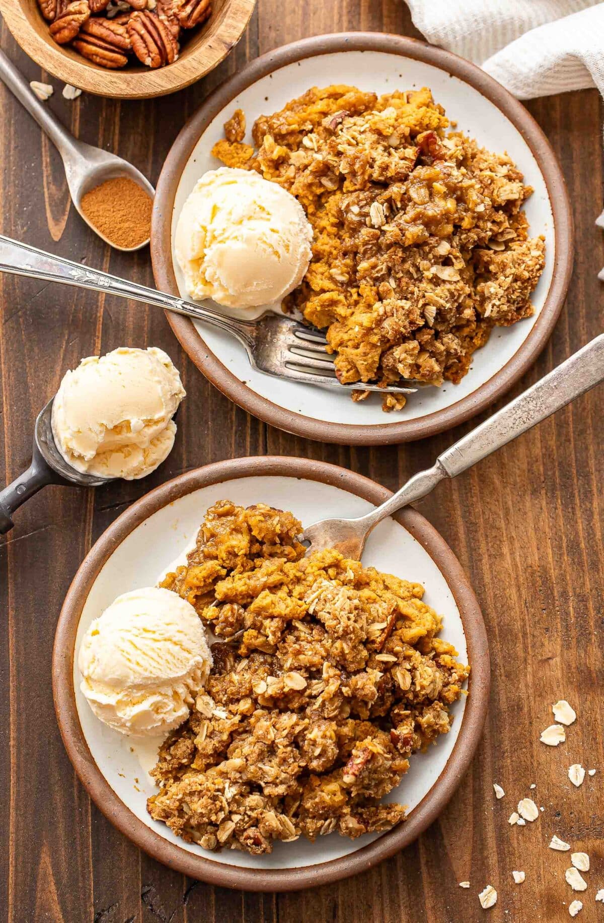 Two white plates with pumpkin crisp and vanilla ice cream on them.