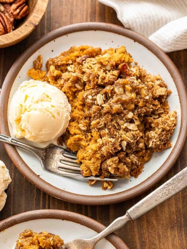 Pumpkin crisp on a white plate with a scoop of vanilla ice cream and a fork.