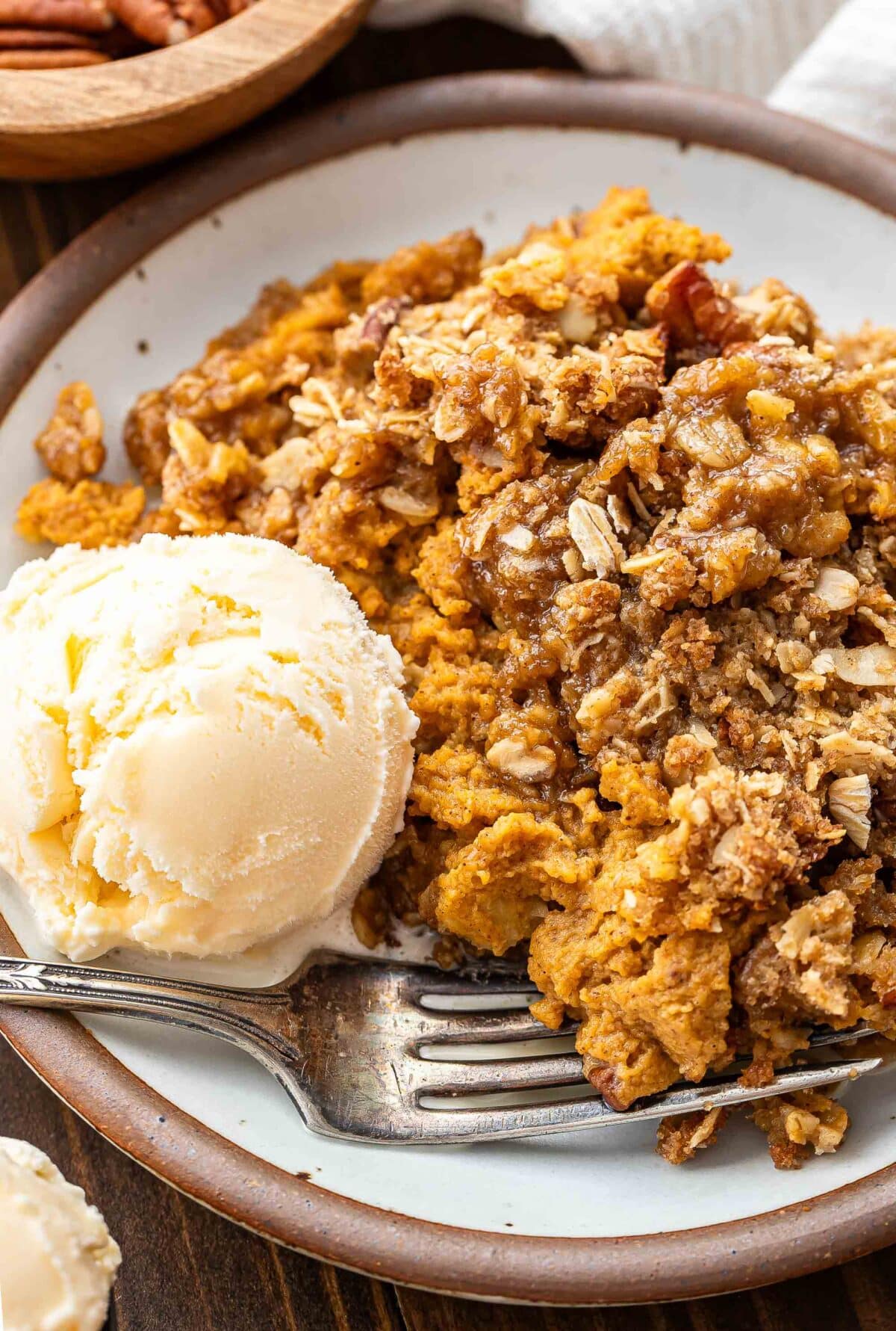Pumpkin crisp on a white plate with a scoop of vanilla ice cream and a fork.