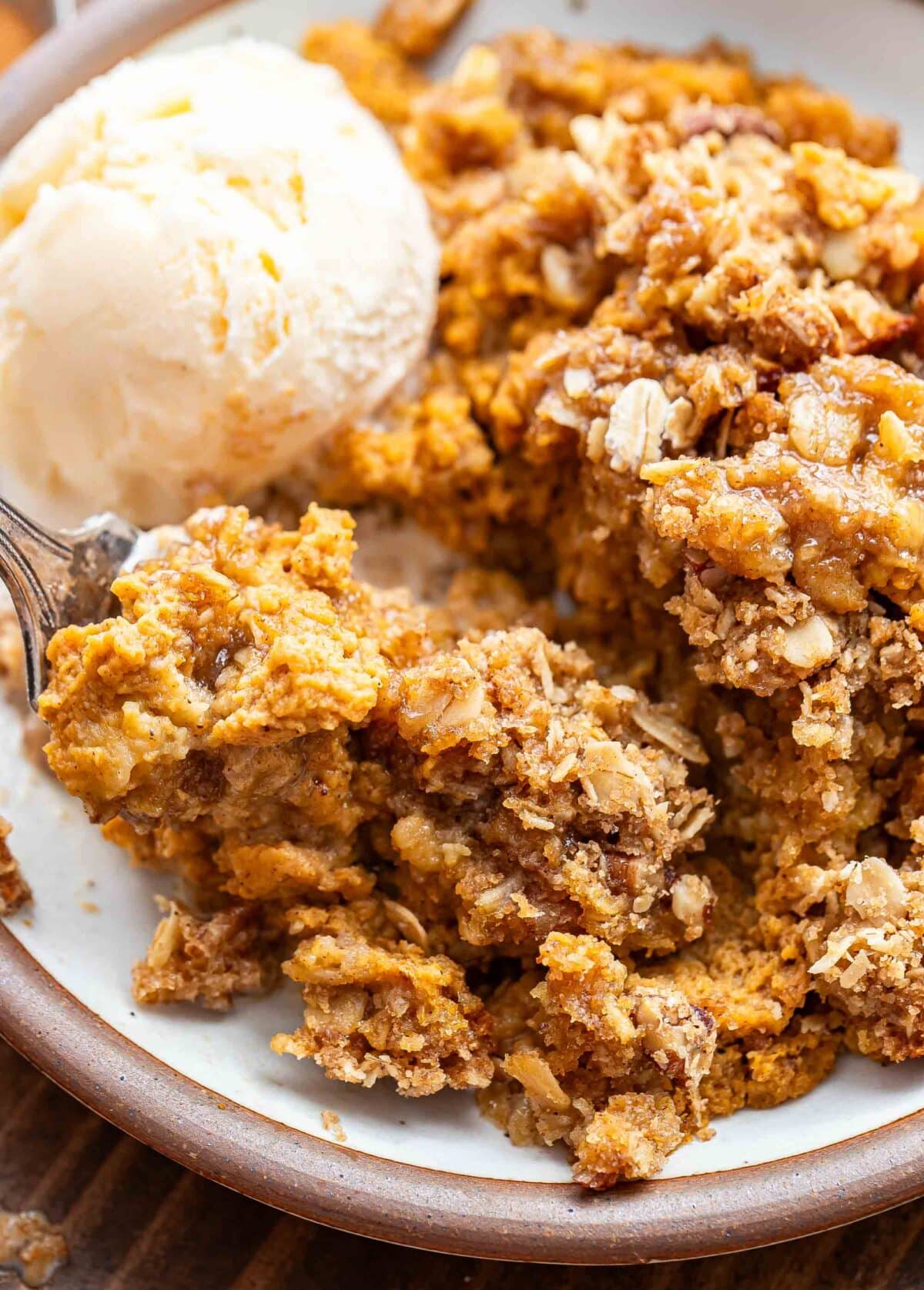 Pumpkin crisp on a white plate with a scoop of vanilla ice cream and a fork.
