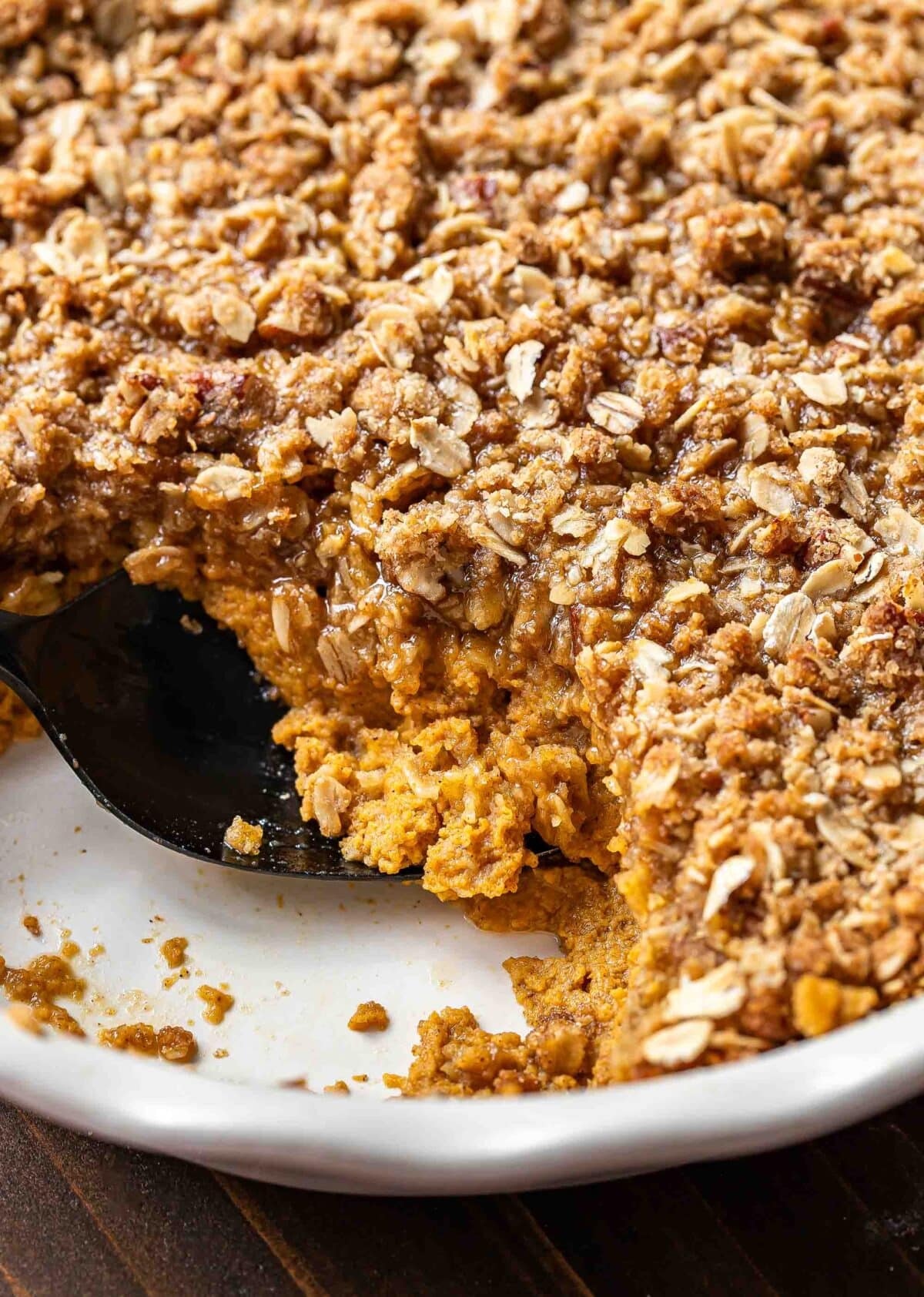 Pumpkin crisp in a white pie dish with a scoop missing.