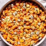 Buffalo Chicken in stainless steel skillet with sweet potato, beans, and blue cheese.
