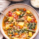 A white bowl filled with Ground Turkey and Vegetable Soup and a bowl of parmesan cheese behind it.