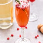 Pomegranate Champagne Cocktail with a sprig of rosemary in the glass and pomegranate seeds.