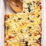 Sausage, Potato, and Kale Breakfast Casserole in a white dish with a square cut out and a wooden spoon in its place