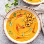 two white bowls full of creamy red lentil soup topped with cashews, cilantro, and sriracha.