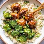 Sesame Chicken Meatballs and broccoli on top of rice in a white bowl with chopsticks.