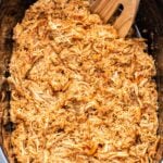 Slow Cooker Barbecue Chicken in a black crockpot with a wooden spoon.