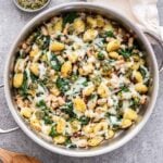 Spinach White Bean Gnocchi in a Skillet with a bowl of pesto behind it and a wooden serving spoon in front.