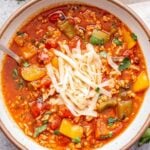 Stuffed Pepper Soup in a white bowl topped with shredded cheese.