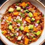 Overhead photo of Lentil Sweet Potato Chili in a white bowl with a halved lime behind it.