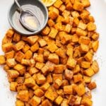 White oval platter with Garam Masala Roasted Sweet Potatoes, a bowl of maple syrup, and a halved lemon on it.