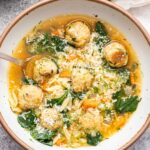 A white bowl full of Italian Wedding Soup with a spoon in it.