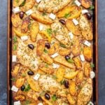 Rimmed sheet pan with Greek chicken and potatoes, feta, and kalamata olives.