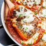 Wooden spoon lifting up a piece of the chicken parmesan out of the marinara sauce.