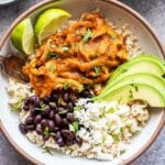 Chicken Tinga Bowl filled with rice, avocado slices, black beans, and lime wedges.