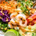 Spring Roll Bowl filled with rice noodles, shrimp, avocado, red cabbage, carrots, cucumbers, and red bell pepper. Drizzled on top with peanut sauce.