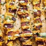 Five Tandoori Chicken Skewers on a sheet pan drizzled with cilantro yogurt sauce.