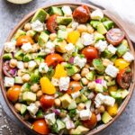 Tomato Avocado Chickpea Salad in a white bowl with a jar of lemon vinaigrette behind it.