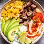 Southwest Steak Bowl topped with cubed grilled steak, grilled corn, peppers, and onions, and slices of avocado.