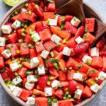 Strawberry Watermelon Feta Salad in a bowl with two wooden spoons and a halved squeezed lime behind it.